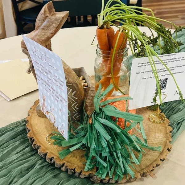 A wooden bunny, carrots in a jar, and cards on a wooden slice centerpiece for an Anchor Point Bistro event.