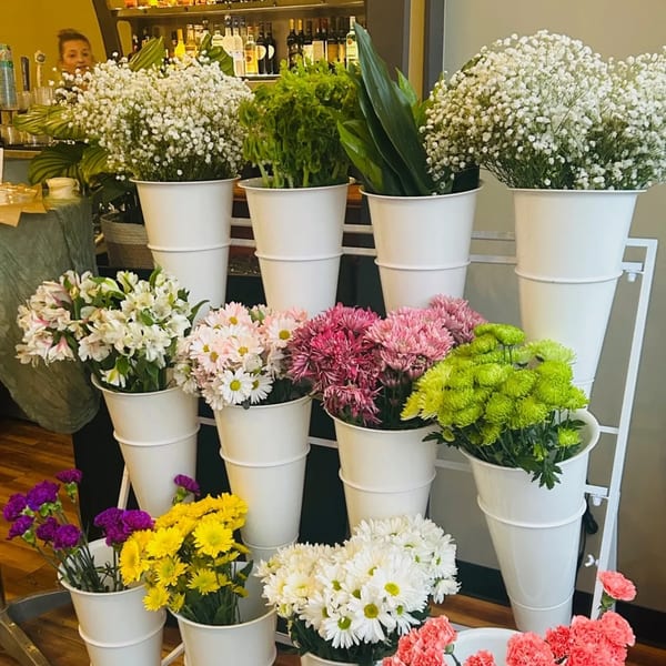 A multi-tiered display of fresh flowers in white buckets, including baby's breath, daisies, and carnations.