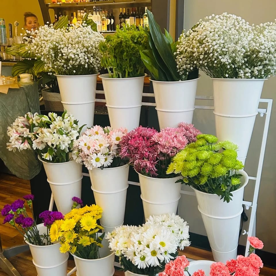 A multi-tiered display of fresh flowers in white buckets, including baby's breath, daisies, and carnations.