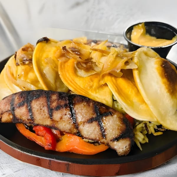Grilled pork chop with bell peppers, pierogies topped with caramelized onions, and a side of cheese sauce.
