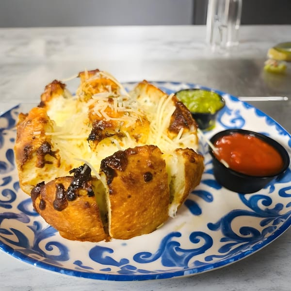 Pull-apart cheesy bread with two dipping sauces on a blue and white patterned plate.